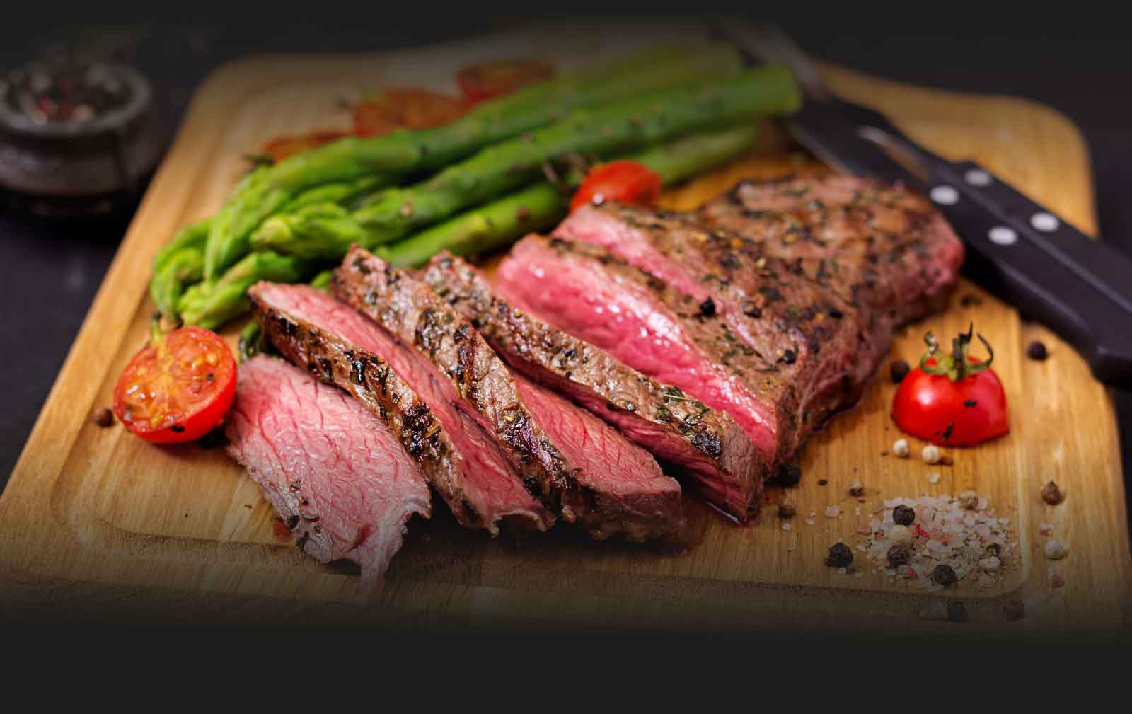 Aufgeschnittenes Steak mit grünem Spargel auf einem Holzbrett